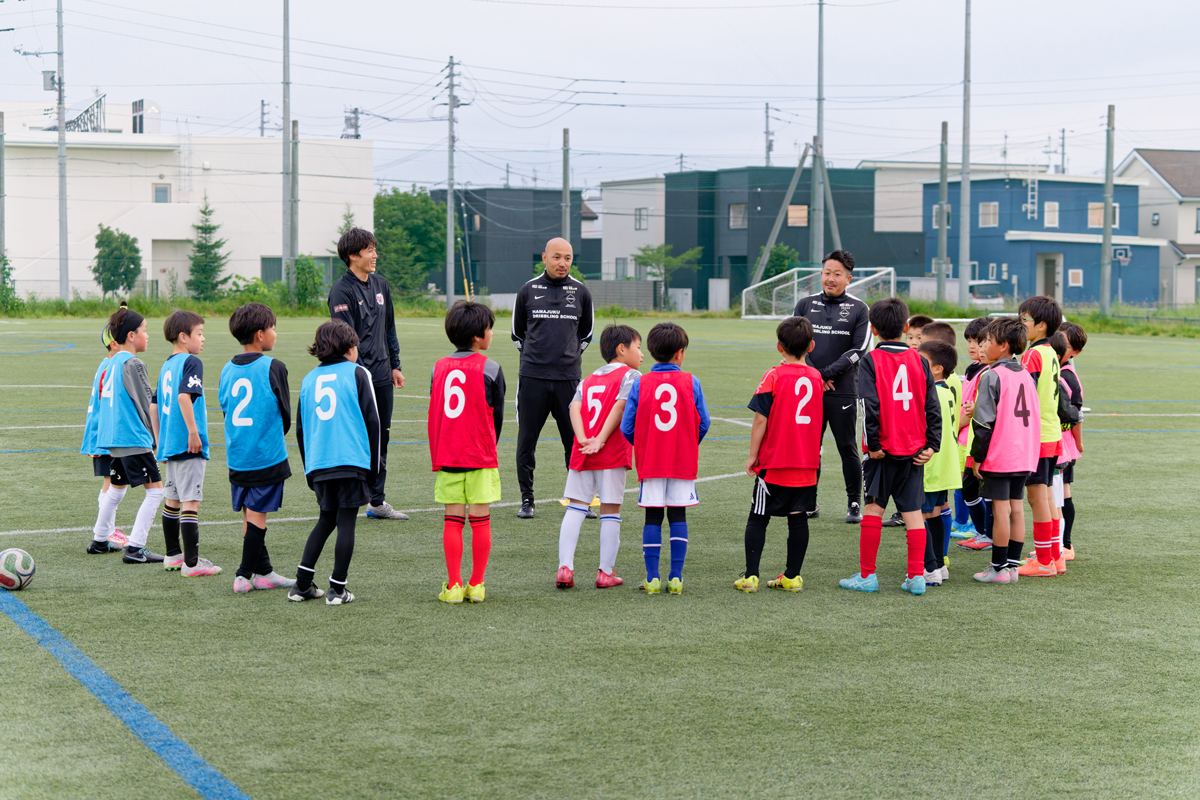 サッカー場でコーチの話を聞く子どもたち